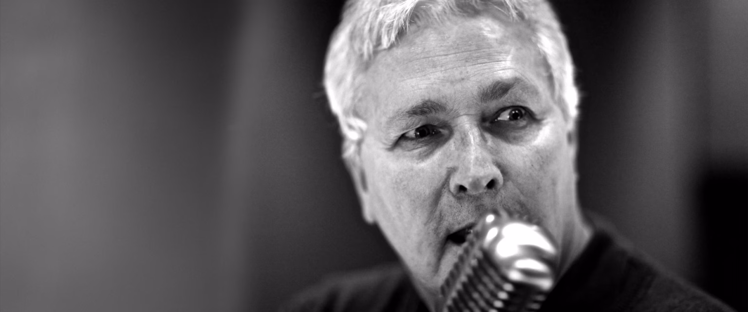 Portrait noir et blanc de Joël Demarty, comédien voix off Sonacom, en pleine prise de voix, au micro vintage