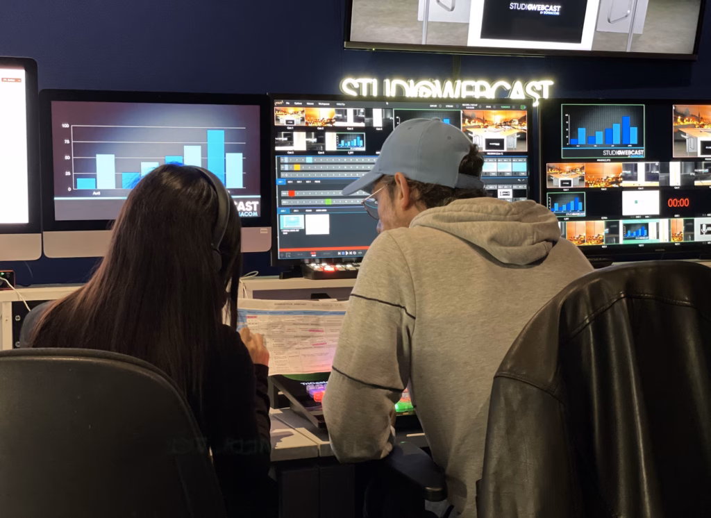 Deux opérateurs de régie devant le mur d'écrans du Studio Webcast