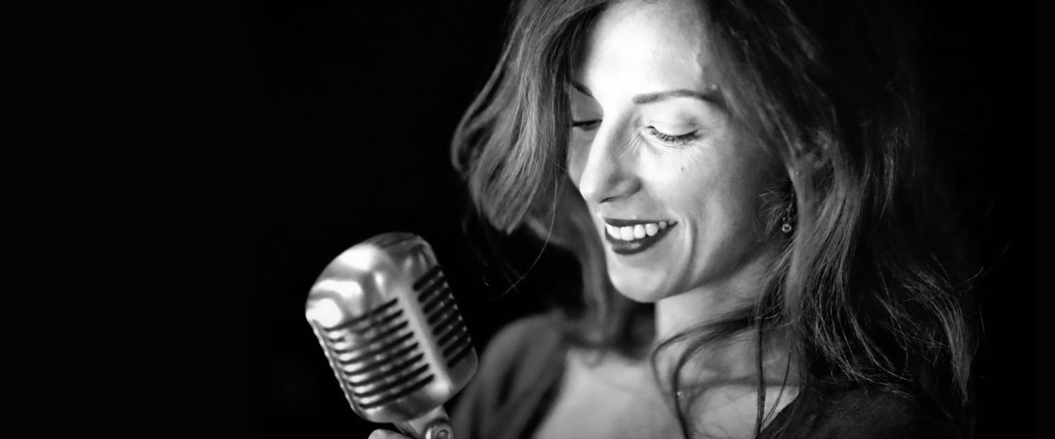 Portrait noir et blanc de Zelda Rittner, comédienne voix off Sonacom, le regard baissé, souriante, au micro vintage