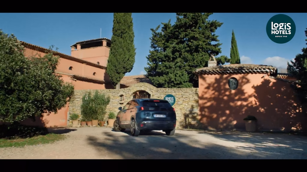 Voiture garée devant un hôtel Logis aux murs ocre, spot TV préparé pour la diffusion par Sonacom